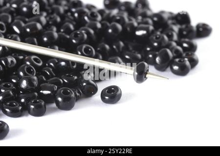 Beads spread on white background with needle. Beads with needle . Close up, macro, It is used in finishing fashion clothes. make bead necklace, beads Stock Photo