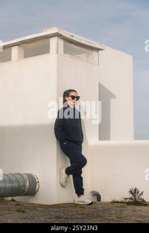 Sporty woman wearing a tracksuit leaning against a white wall resting Stock Photo
