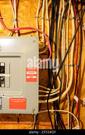 Close-up of a residential circuit breaker panel and wiring routed along the basement wall with a wooden support panel Stock Photo