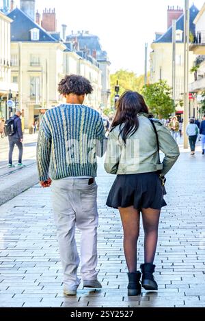 Rear view of young ethnic casually dressed couple walking along city center pavement - Tours, Indre-et-Loire (37), France. Stock Photo