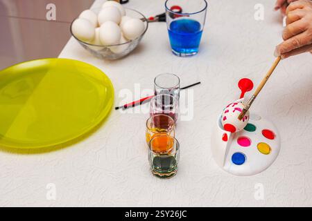 Hand painting Easter egg with colorful dyes on white table with brushes and palette. Sweden. Stock Photo