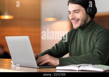 Young positive man in wireless headphones studying online on laptop Stock Photo