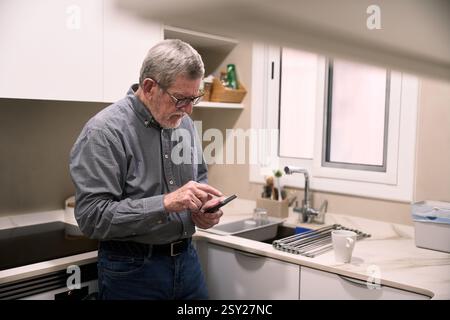 Senior man using smartphone in modern kitchen Stock Photo