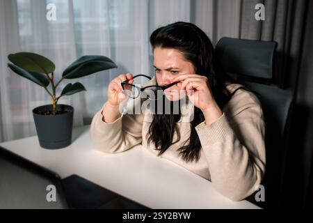 Female with bad eyesight trying to read information from computer using eyeglasses. Freelancer using laptop for work. Stock Photo