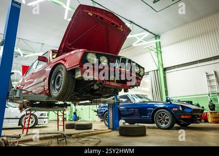 In a fully equipped automotive workshop environment, there are two classic cars being carefully serviced Stock Photo