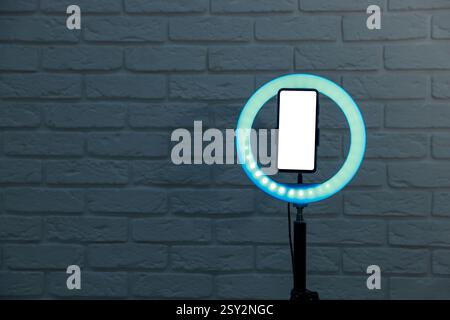 Ring lamp with smartphone against brick wall, space for text Stock Photo