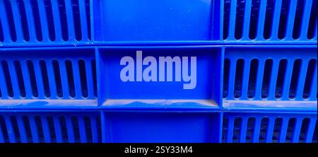 Close up view of a blue plastic crate featuring a grid like pattern with rectangular slits in rows and a solid rectangular section in the center. Stock Photo