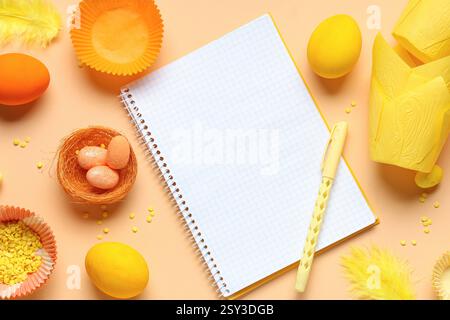 Blank notepad for recipes with pen, Easter eggs and baking molds on orange background Stock Photo
