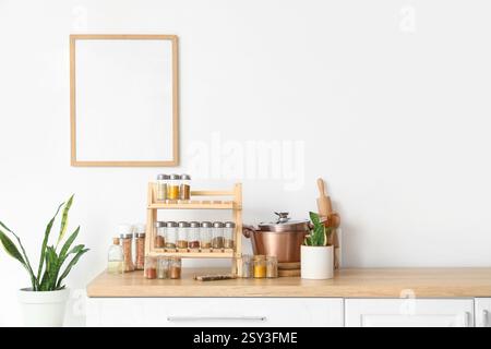 Stand with different spices, utensils and plant on counter near light wall in kitchen Stock Photo