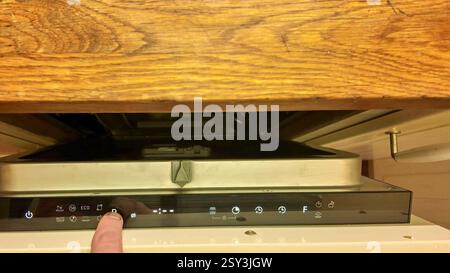 A male finger on the control panel of the dishwasher. Changing cycles on the dishwasher. Illuminated buttons on the dishwasher's digital display Stock Photo