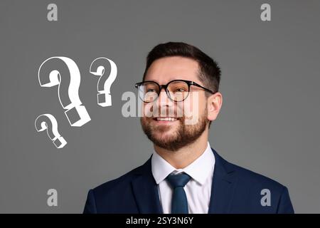 Happy businessman looking at question marks on grey background Stock Photo