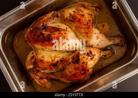 Aromatic oven-baked chicken with a beautifully roasted surface, resting in its juices inside a stainless steel roasting pan. Stock Photo
