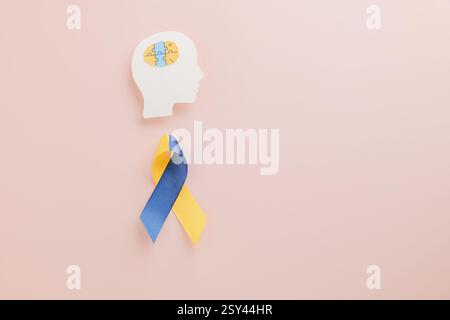 World Down Syndrome Day and Autism Awareness on a bright pink background. A paper head with puzzle pieces and yellow-blue ribbon represents Down Syndr Stock Photo