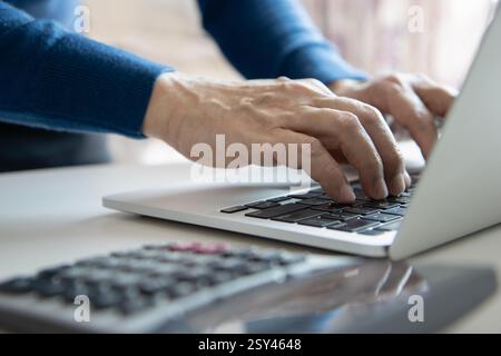 Close up of a man in modern home office typing on a computer notebook or laptop computer while surfing internet  for stock exchange, chatting with cus Stock Photo