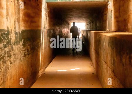 silhouetted figure walks through a dimly lit underpass in Enugu, Nigeria, March 2025. The tunnel's aged walls contrast with the bright exit ahead Stock Photo