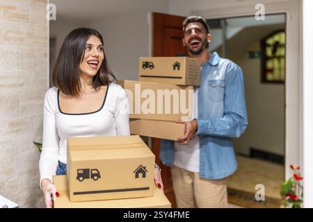 Cheerful homeowners carrying cardboard boxes, smiling as they enter their new apartment, embracing the excitement of their fresh start together Stock Photo