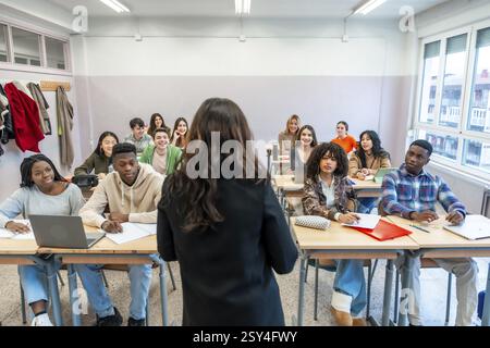 Female professor teaching a lesson to a multi ethnic group of students sitting at desks in a classroom Stock Photo