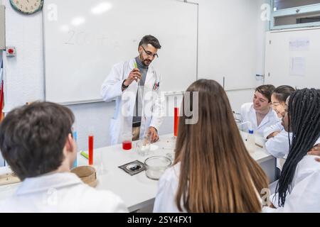 Chemistry teacher performing a chemical experiment with students in a university laboratory, using lab coats and equipment Stock Photo