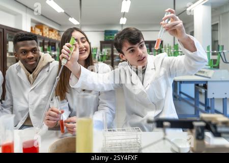 Young chemistry students wearing lab coats performing experiment using test tubes and other laboratory equipment Stock Photo