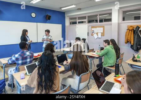 Multi ethnic group of high school students attending a lesson with two teachers and using laptops in a modern classroom Stock Photo