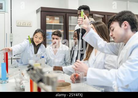 University students in lab coats conducting a chemistry experiment using colorful liquids and lab equipment Stock Photo