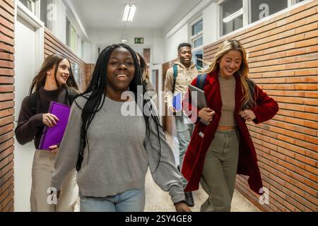 Cheerful multi ethnic university students walking together in a bustling school corridor, sharing laughter and enjoying their college experience Stock Photo