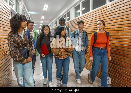 Multi ethnic university students walking down school hallway, chatting and holding books and tablets Stock Photo