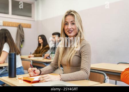 Blonde female college student taking notes and engaging in learning during a university lesson in a focused classroom environment Stock Photo