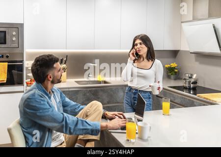 Young couple working remotely in their modern kitchen, enjoying breakfast while managing their professional tasks Stock Photo