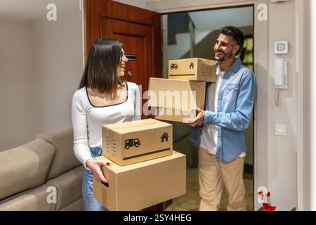 Young couple carrying cardboard boxes while entering their new home, smiling and looking at each other Stock Photo