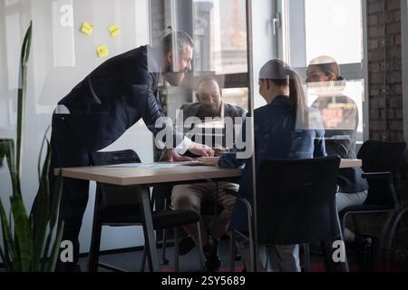 Business meeting in modern office with diverse professionals discussing documents at a table. Concept of teamwork, leadership, collaboration, and Stock Photo