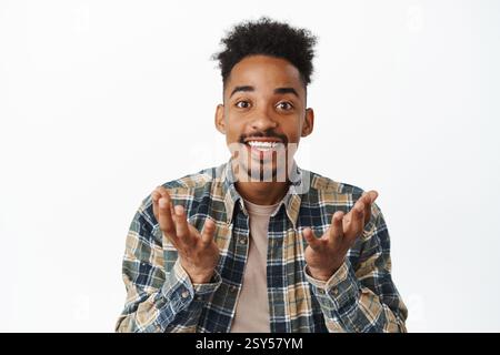 Close-up portrait of a happy African American man looking surprised and proud of you, raising hands as if holding something in empty palms, making an announcement. Stock Photo