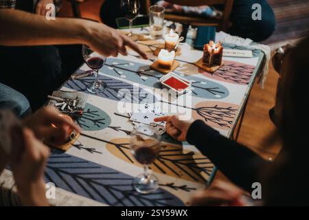 Friends playing cards together enjoying a cozy atmosphere with candles and wine Stock Photo