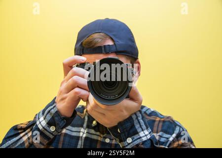 A male photographer in the process of taking pictures, on a yellow background. Stock Photo
