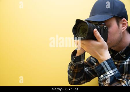 A male photographer in the process of taking pictures, on a yellow background. Stock Photo