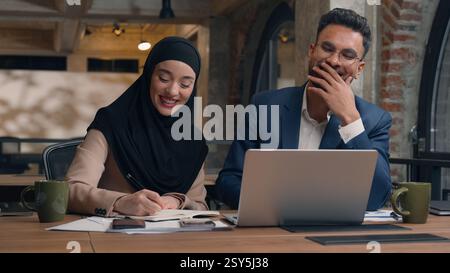 Two business colleagues co-workers talk discuss corporate work at office cafe multiracial male female employees Indian man muslim woman in hijab Stock Photo