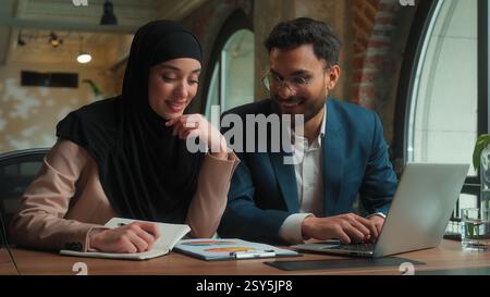 Male female teamwork Arabian man muslim woman in hijab girl guy businessman businesswoman two happy business colleagues coworkers managers analyzing Stock Photo