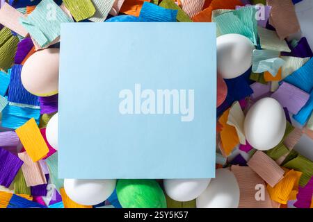A blank yellow notebook surrounded by colorful eggs and vibrant pieces of paper for Easter celebration. Stock Photo