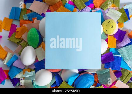 A blank yellow notebook surrounded by colorful eggs and vibrant pieces of paper for Easter celebration. Stock Photo