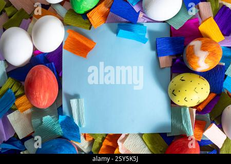 A blank yellow notebook surrounded by colorful eggs and vibrant pieces of paper for Easter celebration. Stock Photo