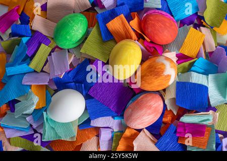Decorative Easter eggs painted in vibrant colors and scattered among colorful crepe paper. Perfect for festive celebrations, Easter. Stock Photo