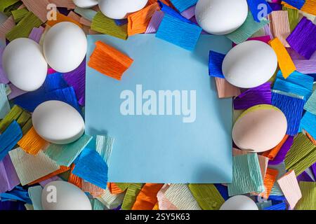 Easter greeting card. Top view of white eggs with multi-colored crepe paper background, blue card for text. Stock Photo
