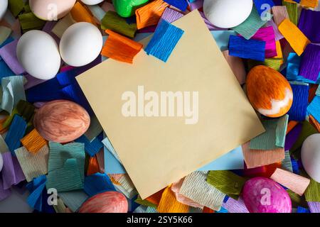 A blank yellow notebook surrounded by colorful eggs and vibrant pieces of paper for Easter celebration. Stock Photo