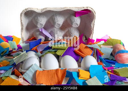 Brightly colored paper pieces scattered around white eggs in a cardboard box. Perfect for celebrations, festive marketing materials. Stock Photo