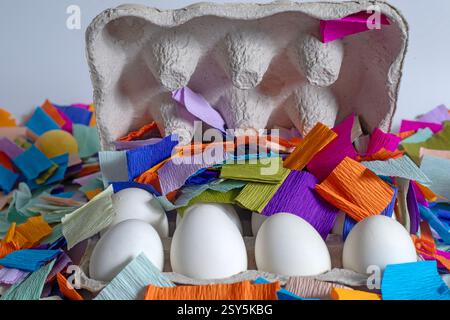 Brightly colored paper pieces scattered around white eggs in a cardboard box. Perfect for celebrations, festive marketing materials. Stock Photo