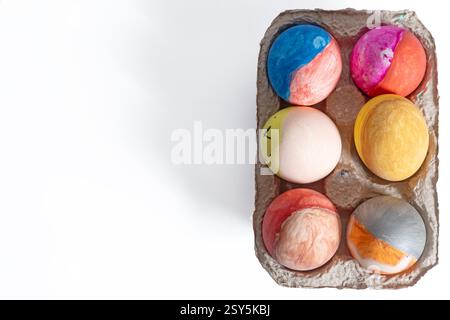 Hand-painted Easter eggs with vibrant patterns and designs arranged in a cardboard box on a white surface. Stock Photo