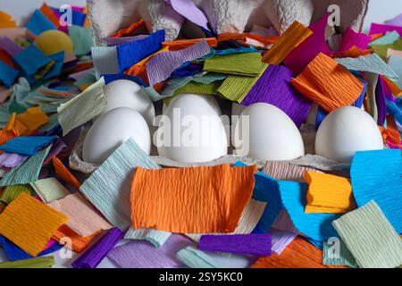 Brightly colored paper pieces scattered around white eggs in a cardboard box. Perfect for celebrations, festive marketing materials. Stock Photo