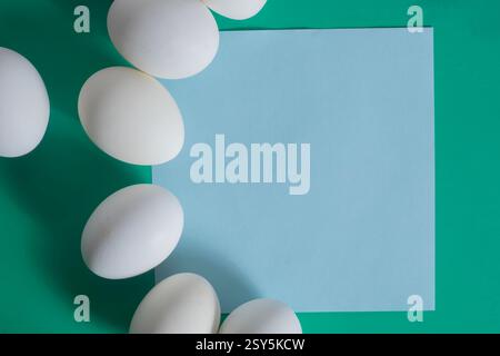 White eggs arranged symmetrically on a vibrant green surface around a blue square paper background. Stock Photo