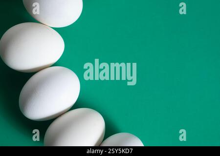 White eggs are artfully arranged on a clean green surface with copy space for text. Stock Photo