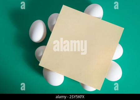 Happy Easter. A blank sheet of paper placed on top of a white egg placed on a vibrant green background. Stock Photo